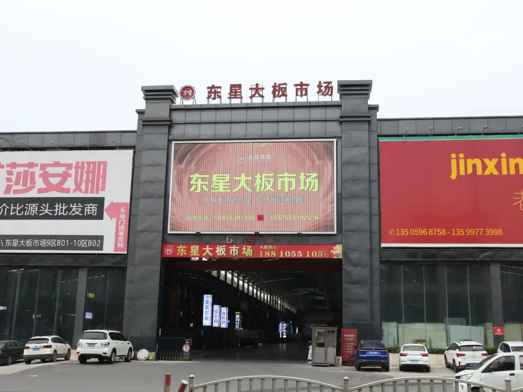 Dongxing Large Slab Market, Shuitou – A major stone trading center in China, featuring a large white roof, black facade with brand ads, and urban surroundings.
